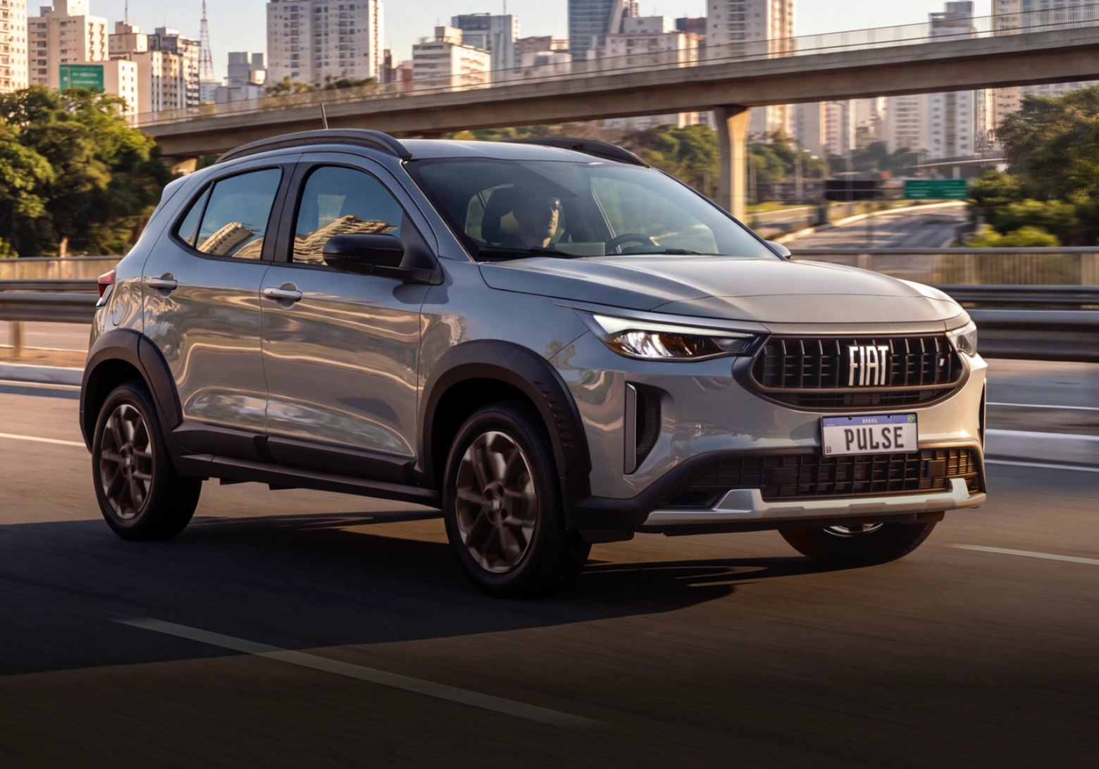 Visão três quartos dianteira do Fiat Pulse cinza em movimento em via elevada, com skyline urbano ao fundo.