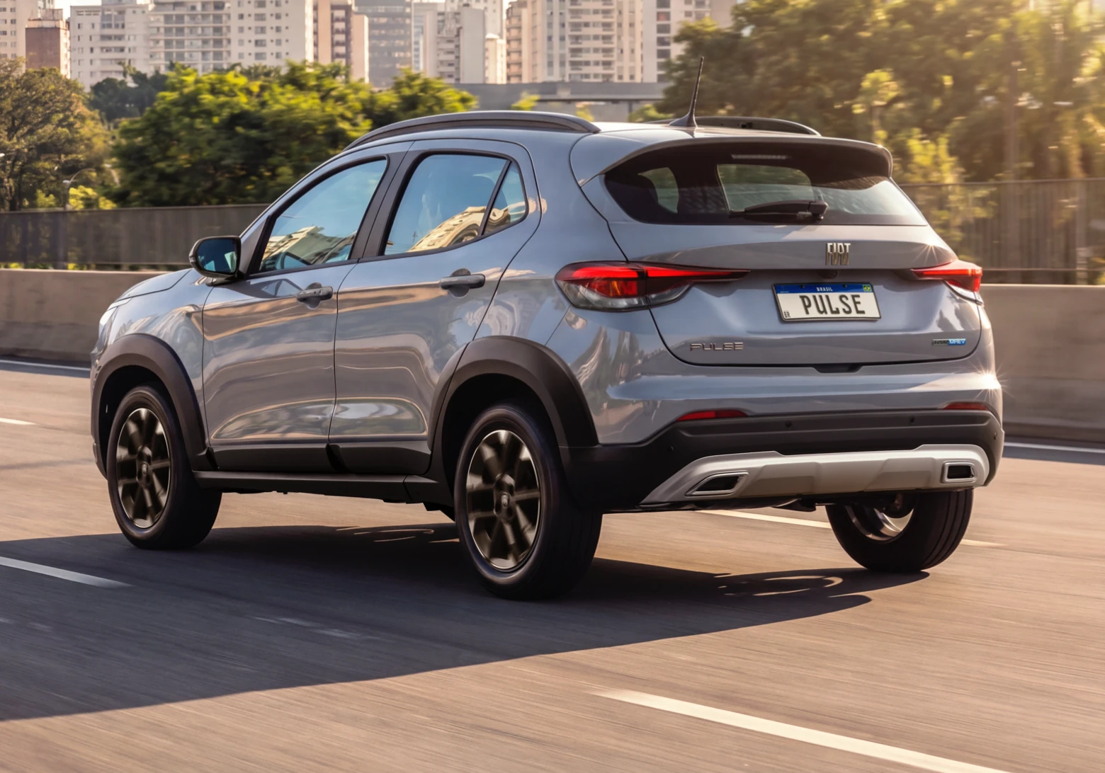 Vista três quartos traseira do Fiat Pulse cinza em movimento em via elevada, com skyline urbano ao fundo.