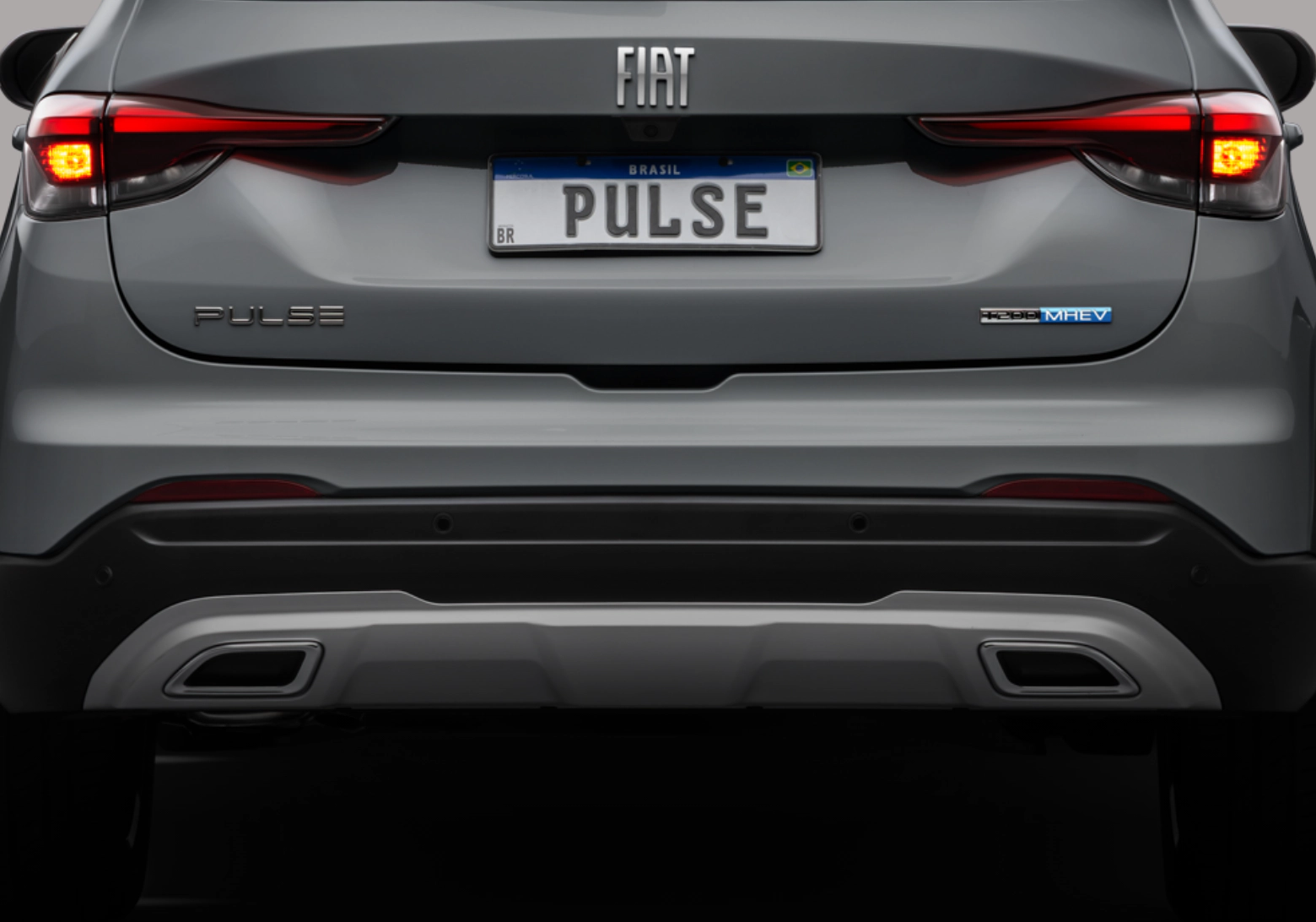Vista traseira do Fiat Pulse cinza com os selos PULSE e T200 MHEV e as lanternas acesas.